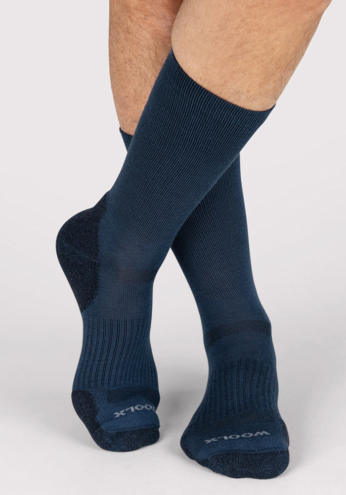 A person wearing Woolx Mens Harbor Crew Socks in Majolica Blue, featuring reinforced heels and toes. The word "WOOL" appears on the toes against a plain, light-colored background.