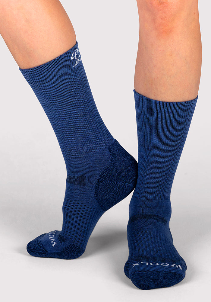 A person wearing Woolx Womens Harbor Crew Socks in Sailor Blue stands on a light gray surface, with one foot flat and the other slightly raised and angled inward.