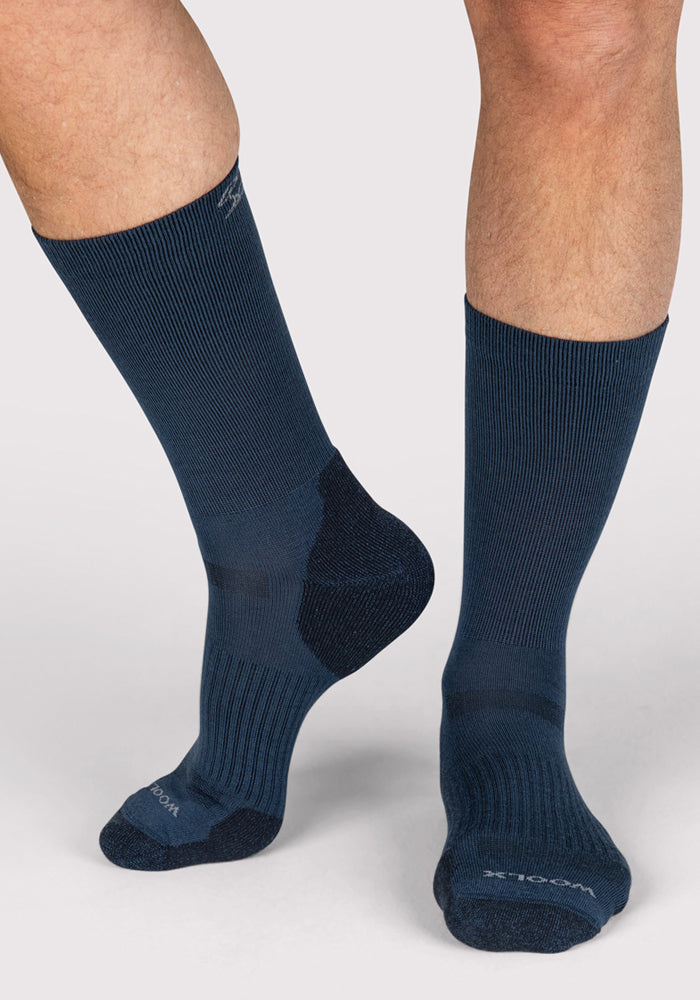 A pair of legs wear Woolx Mens Harbor Crew Socks in Majolica Blue, featuring a ribbed texture. One foot is flat, the other slightly raised, against a light grey background. These Merino wool socks provide moisture-wicking comfort and style.