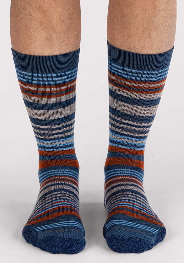 A pair of feet wear Woolx Mens Everyday Crew Socks in Majolica Blue Stripe with blue, gray, orange, and white stripes. The cushioned crew socks reach mid-calf against a plain light-colored background.