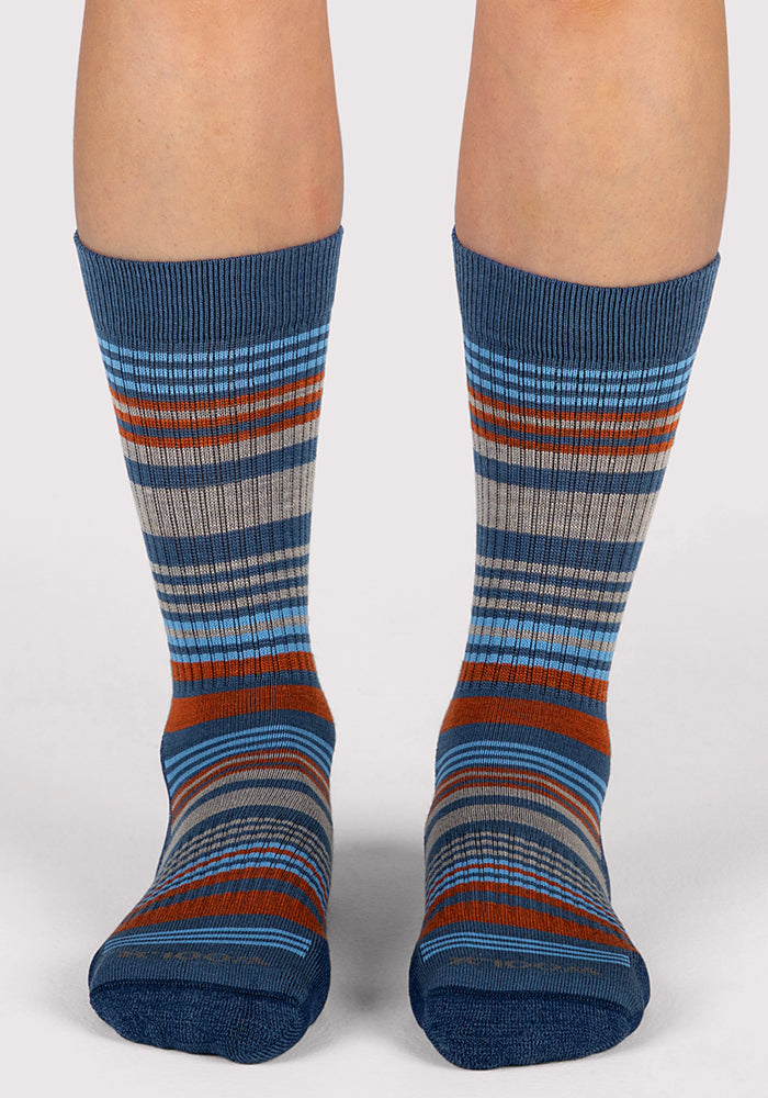 A pair of feet display the Woolx Womens Everyday Crew Socks in Majolica Blue Stripe, featuring blue, gray, orange, and light blue stripes, shown from the front against a plain light background.
