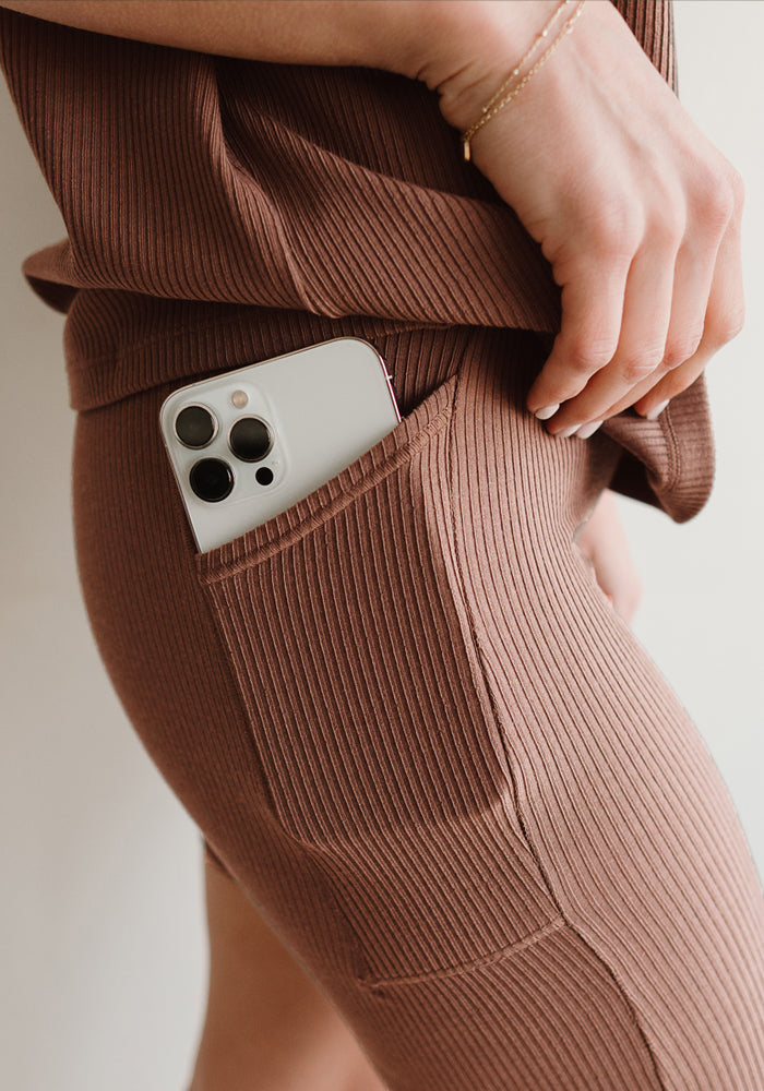 A person wearing Woolx Miley Bike Shorts in Sienna Kiss with a smartphone partially tucked into the pocket, showcasing a close-up of the pocket and phone.