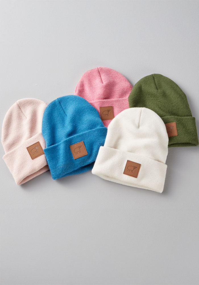 Five Woolx Kids Baylor Beanies in Whipped Cream are displayed on a gray surface, each featuring a brown rectangular patch with a simple design—perfect as warm winter hats for kids.