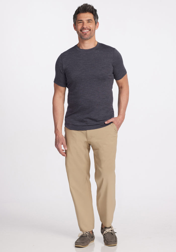 A smiling man stands against a white background, wearing the Woolx Endurance Tee in Cinder Melange, beige pants, and brown boat shoes, with one hand in his pocket.