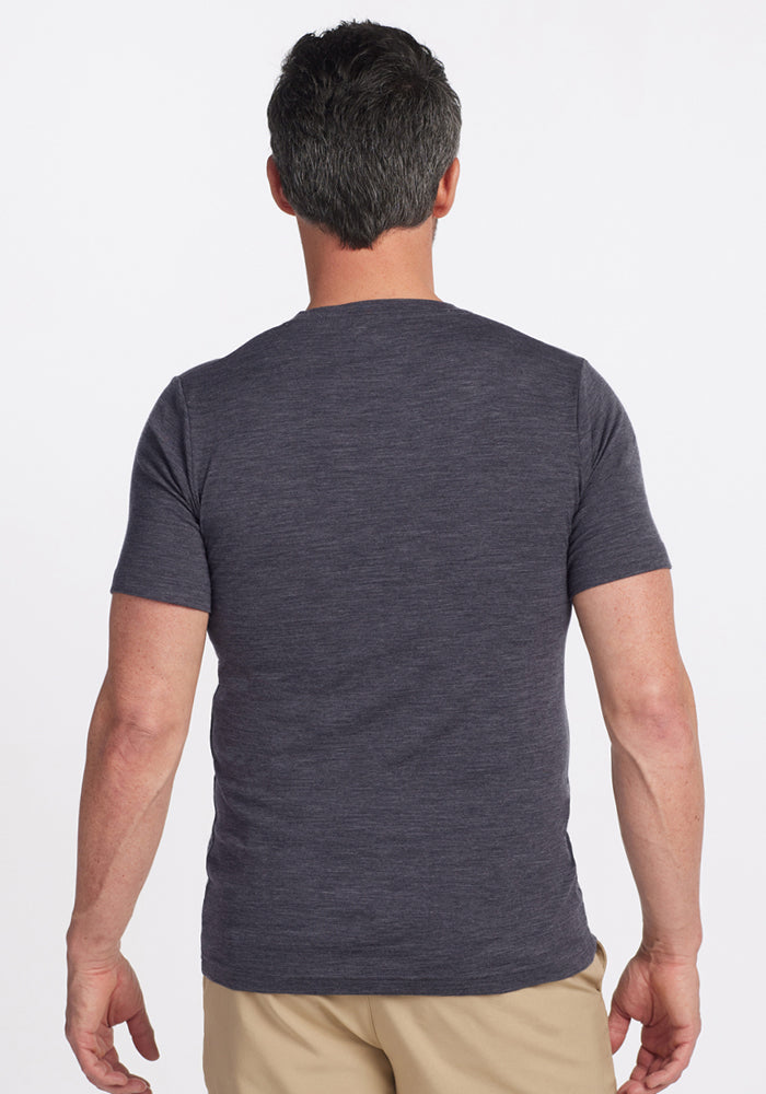 A man with short dark hair, seen from the back, is wearing a Woolx Endurance Tee in Cinder Melange and light-colored pants against a plain white background.