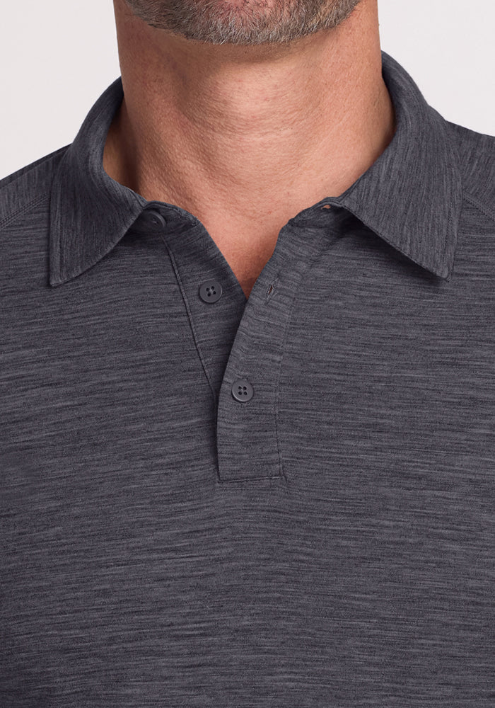 Close-up of a person wearing the Woolx Summit Polo in Cinder Melange, a dark gray, short-sleeve Merino wool button-up with subtle texture. Two buttons are fastened; only the lower face, neck, and upper chest are visible.