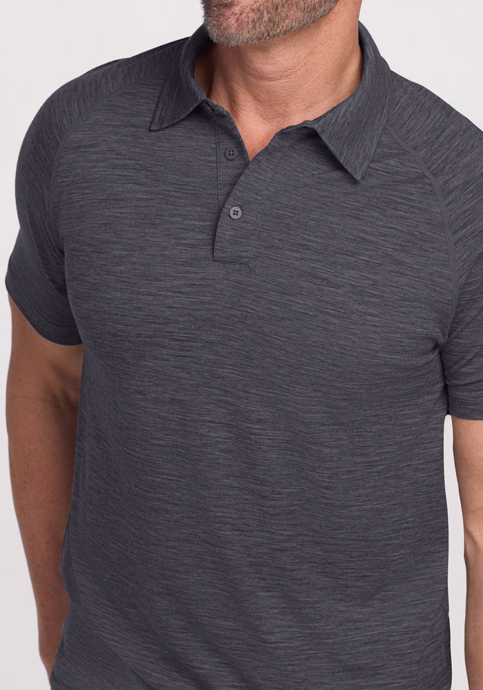 A man wears the Woolx Summit Polo in Cinder Melange, standing against a light background with his head slightly turned, showcasing the shirt’s exceptional moisture management.