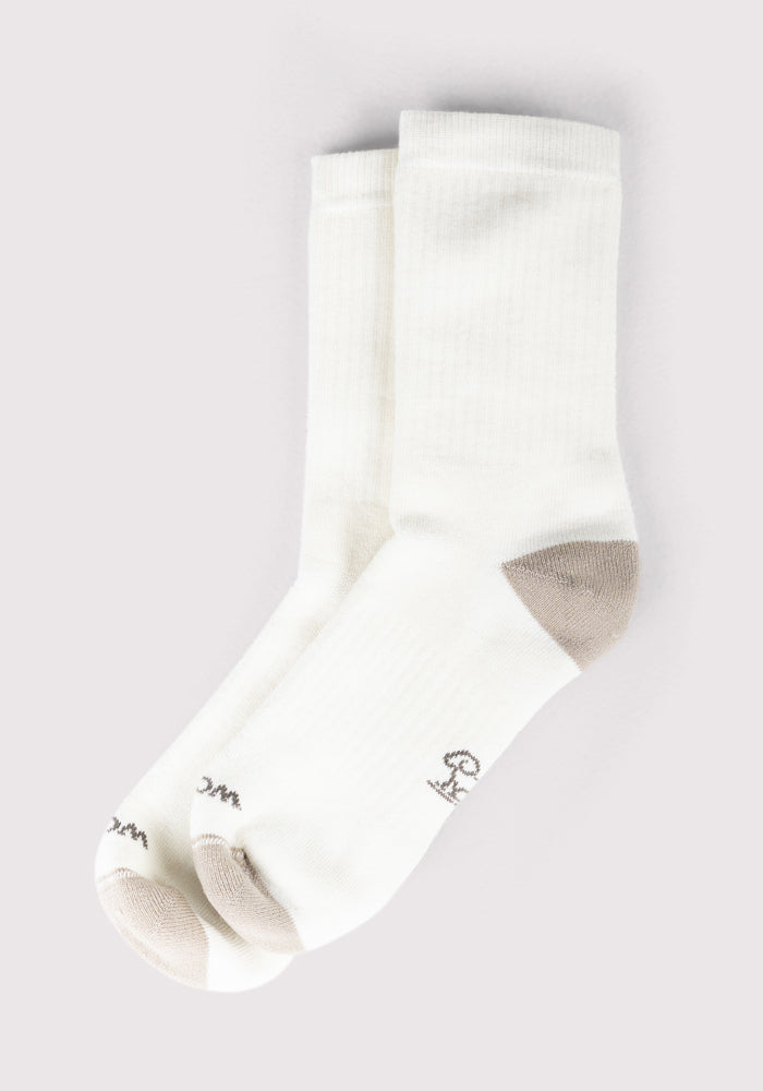 A pair of Woolx Womens Core Crew Socks in Natural, featuring light gray toes and heels and small embroidered logos and text near the toes, are laid flat on a light background.