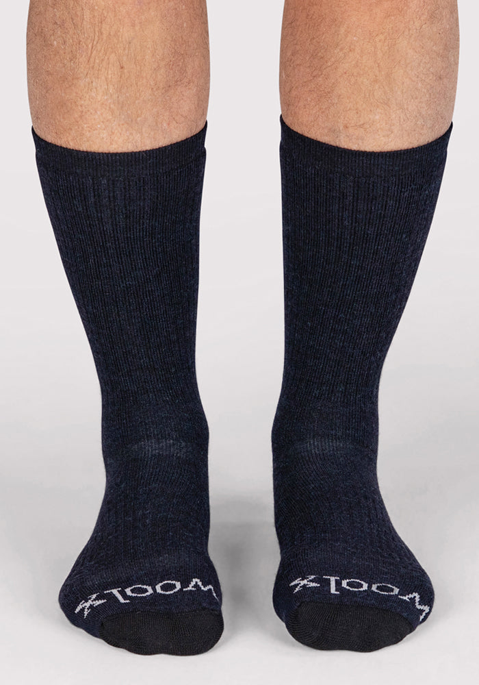 A pair of feet wear Woolx Mens Core Crew Sock in navy, featuring "WOOL" in white near the toes. Made from moisture-wicking Merino wool, the socks are shown against a plain, light background.