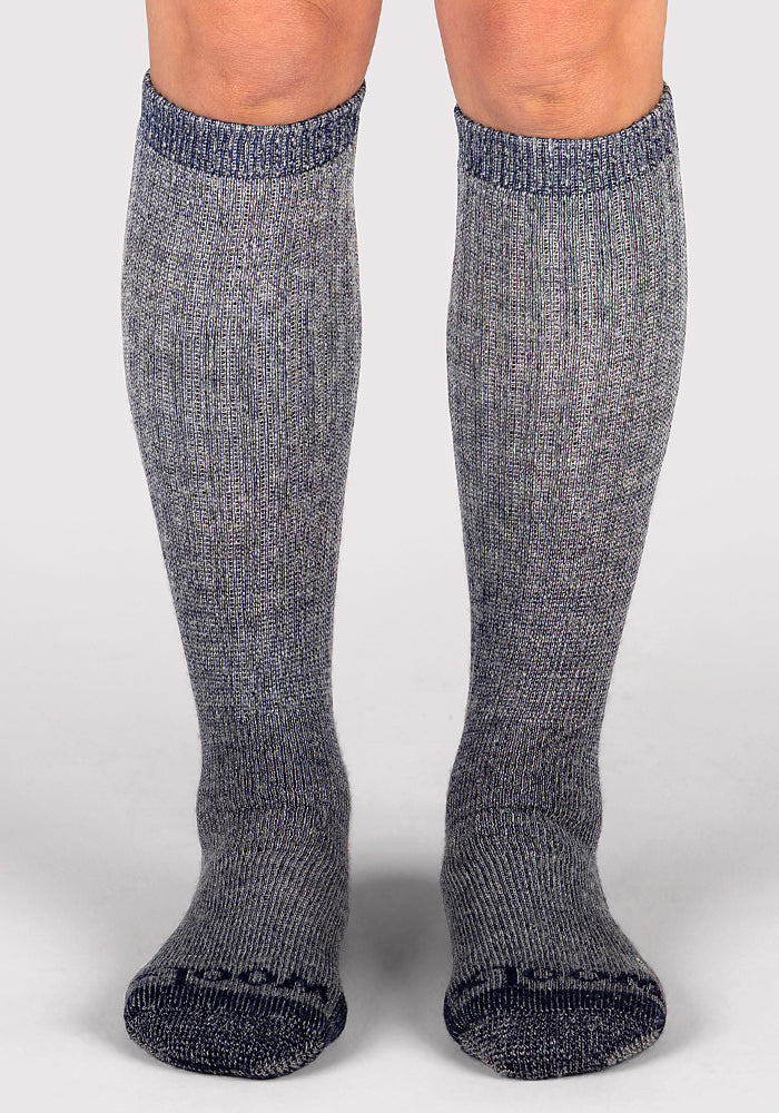 A person is wearing Woolx Womens Extreme Over The Calf Socks in Navy Carbon, standing on a light surface with feet facing forward.