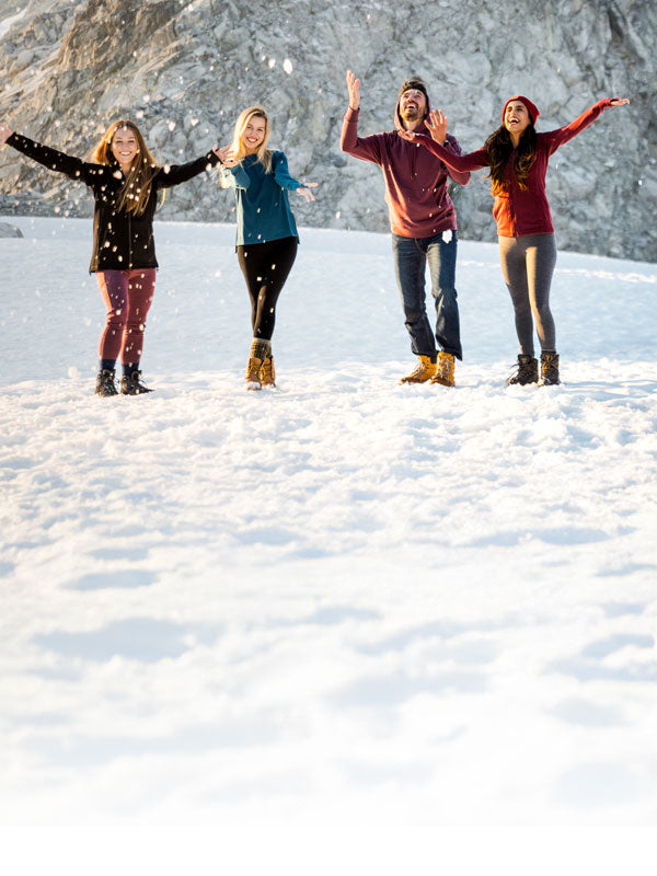 Four people standing in the snow with arms outstretched, enjoying a winter day mobile size
