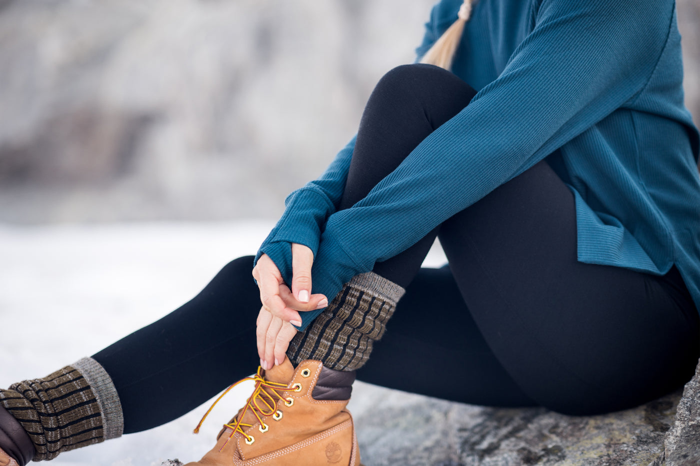 Model wearing black Stella leggings with blue Ainsley top sitting in snow and Joey socks