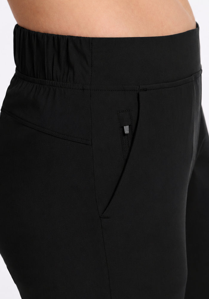 Close-up of a person wearing Woolx Nicole Crop - Black pants, featuring an elastic waistband and front pocket.