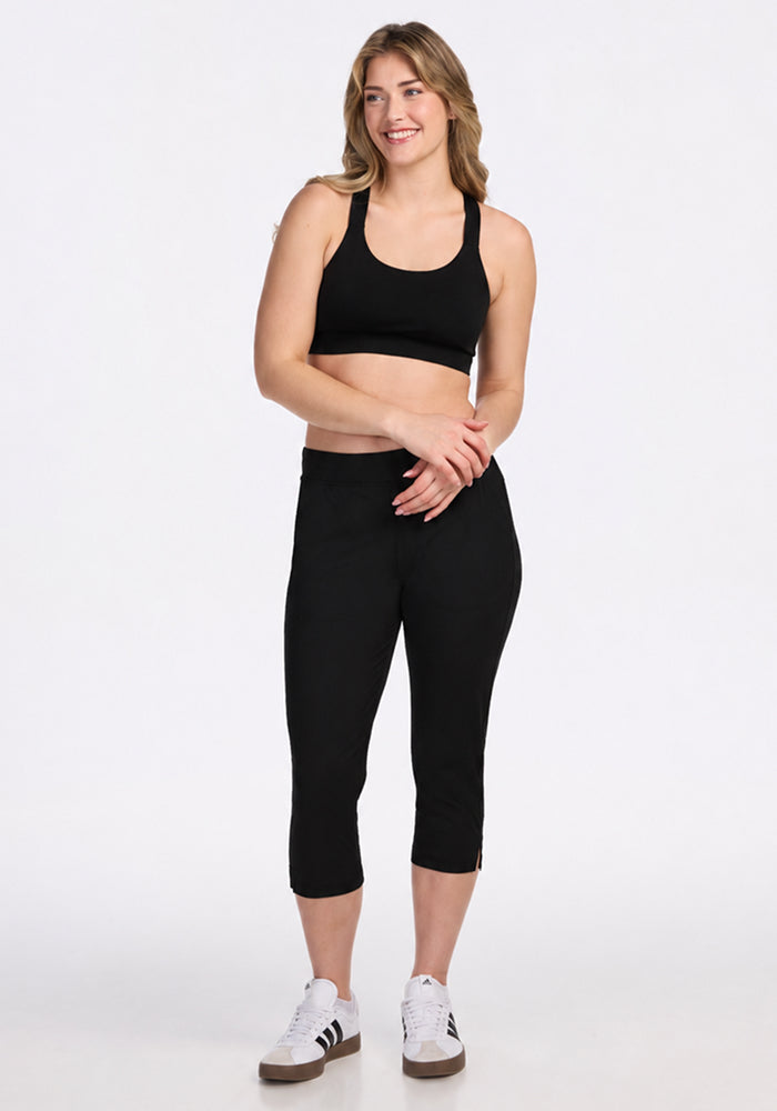 Woman smiles in Woolx Nicole Crop - Black sports bra and pants, wearing white sneakers against a plain background.