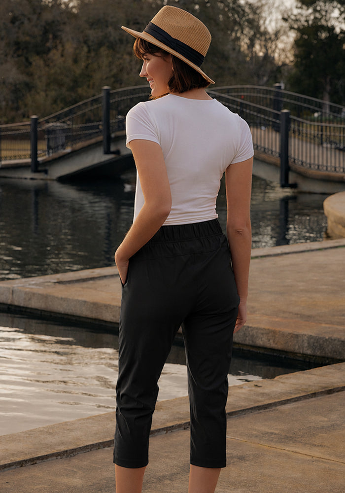 Woman in Woolx Nicole Crop - Black and hat stands by water with a bridge and trees in the background.