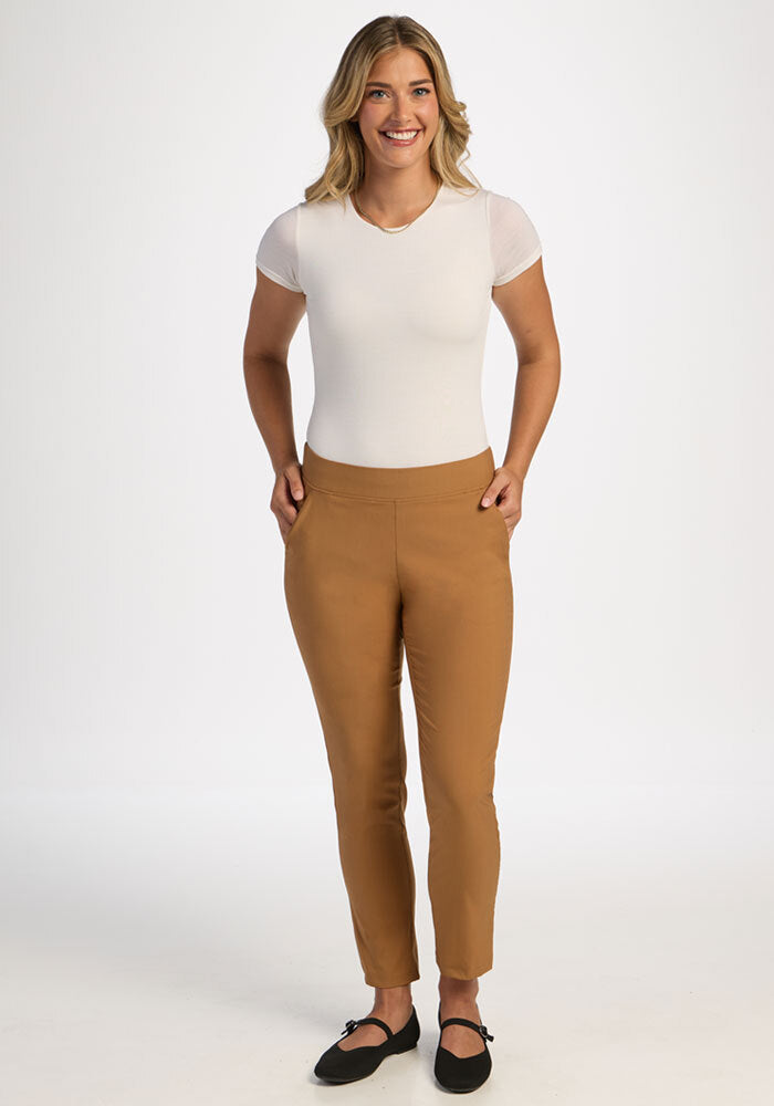 Smiling person in a white top, Woolx Nicole Ankle Pants - Saddleback, and black flats on a white background.