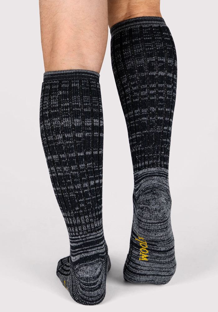 A person wearing Woolx Mens Joey Mid Calf Socks in Dark Navy Marled stands on a light gray background, legs visible from knees down with feet slightly apart.