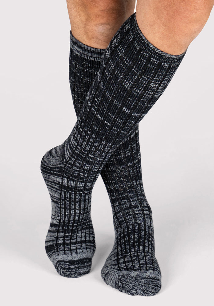 A person wearing Woolx Mens Joey Mid Calf Socks in dark navy marled stands with legs crossed against a plain light background.
