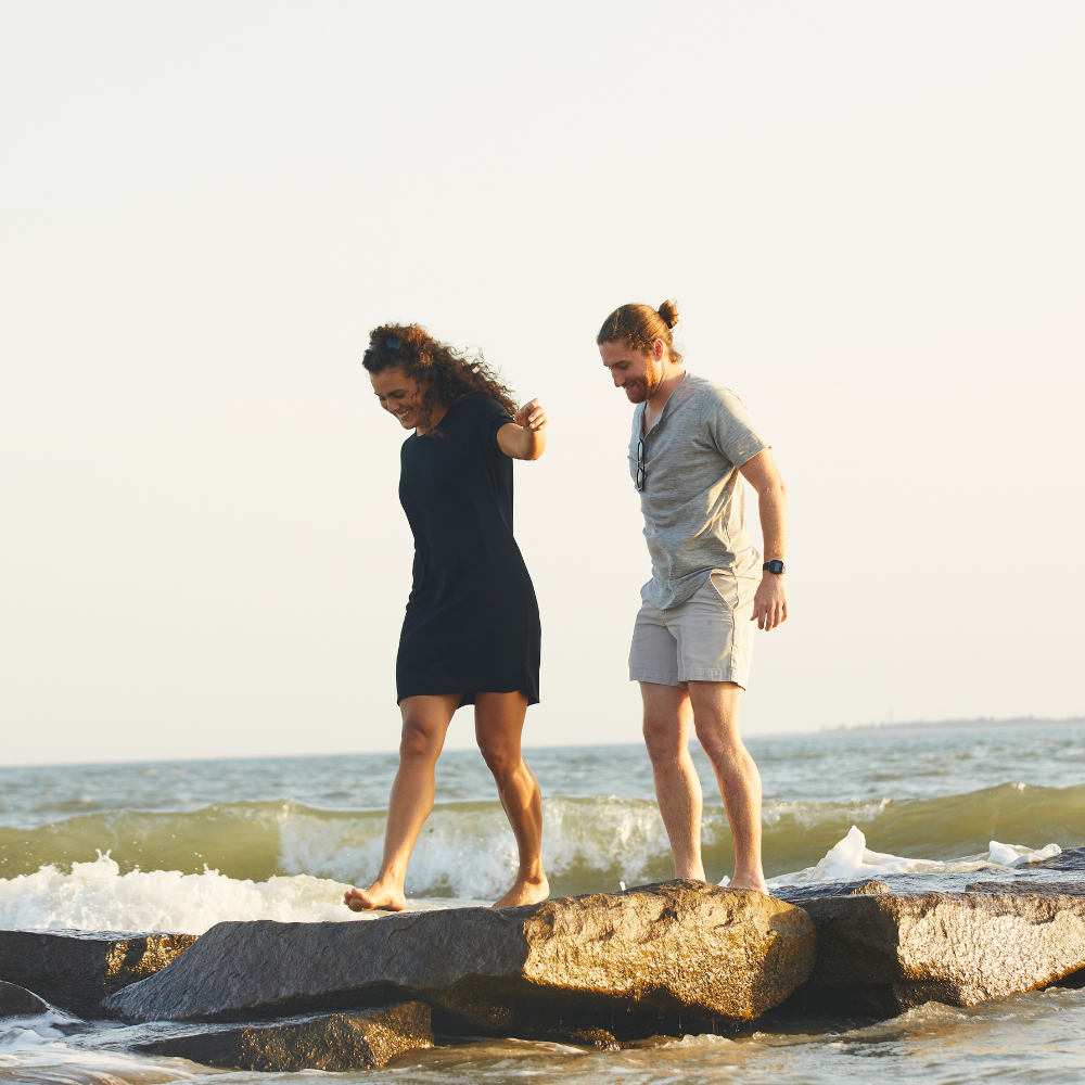 Two people standing on rocks by the ocean with a clear sky.
