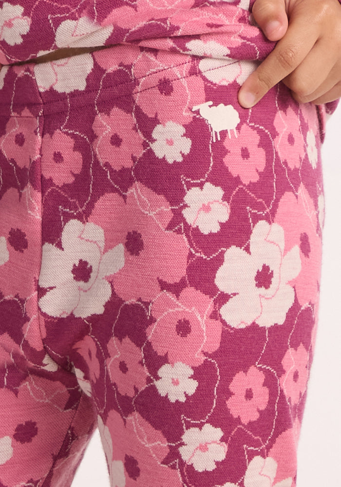 A close-up of a child wearing Woolx Kids Explorer Base Layer Bottoms in the Rosie Posie floral pattern, showing the white sheep logo near the waistband and one hand resting on their hip.