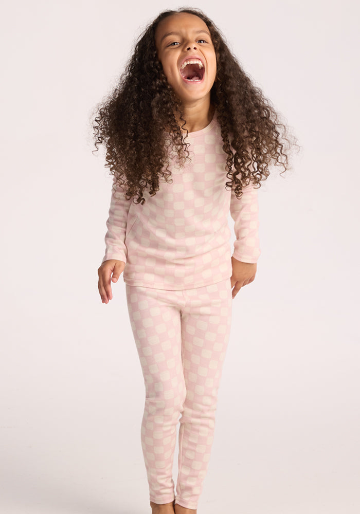 A girl makes a funny face while wearing Woolx Kids Explorer Base Layer Bottoms in Hopscotch Pink, her cozy thermal underwear.
