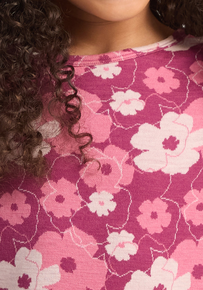 Close-up of the Woolx Kids Explorer Base Layer Top in Rosie Posie, a pink and magenta floral-patterned sweater made from soft Australian Merino wool, with curly brown hair and part of a child's chin visible at the top.