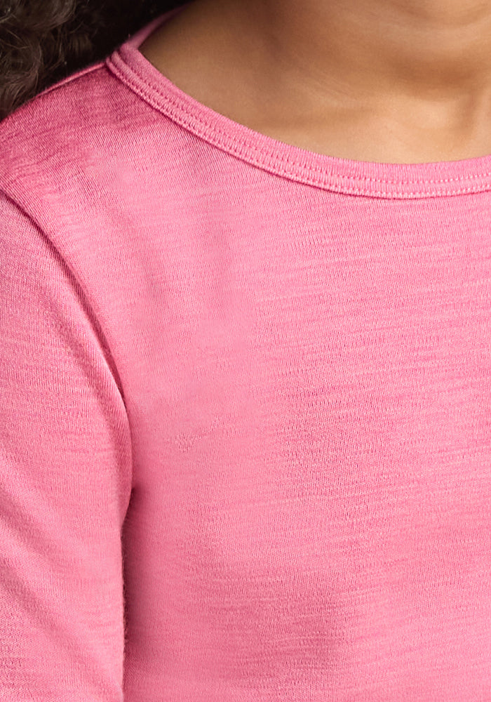 A close-up of a child in the Woolx Kids Explorer Base Layer Top - Pinky Promise shows the shoulder, neckline, and chest. The soft Australian Merino wool fabric provides moisture-wicking comfort. The lower half of the child's face is partially visible.