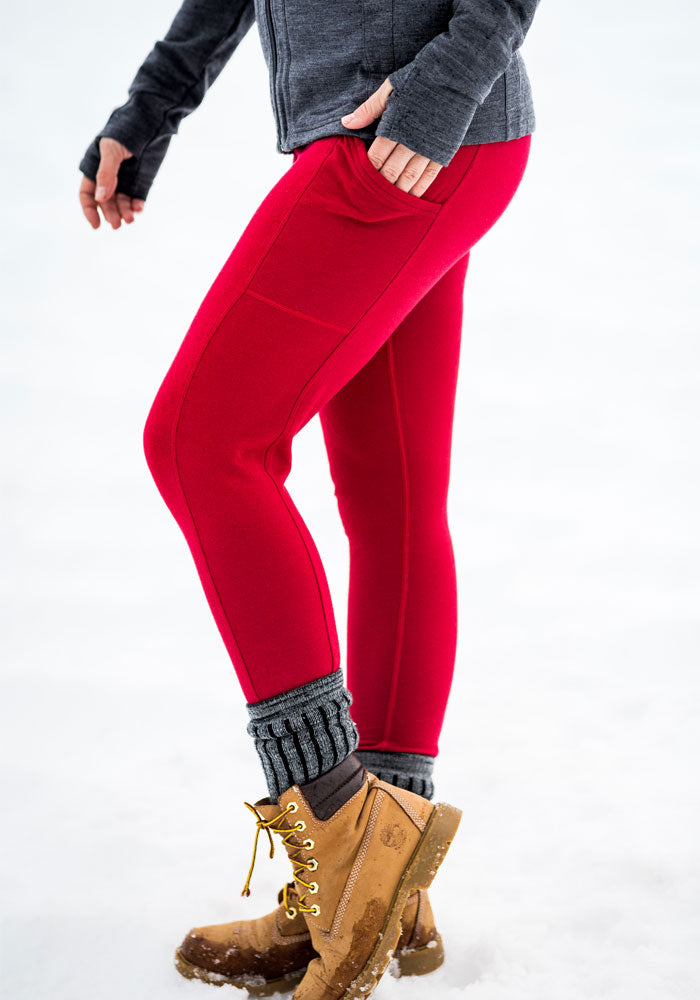 Lower body in Woolx Piper Pocket Leggings - Maraschino Cherry, gray top & socks, tan boots, standing on snow.