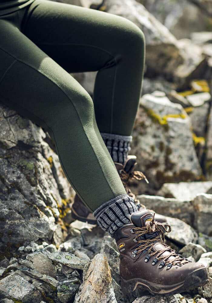 Person in Woolx Piper Pocket Leggings - Duffel Bag, moisture-wicking socks, and hiking boots sits on rocky terrain.