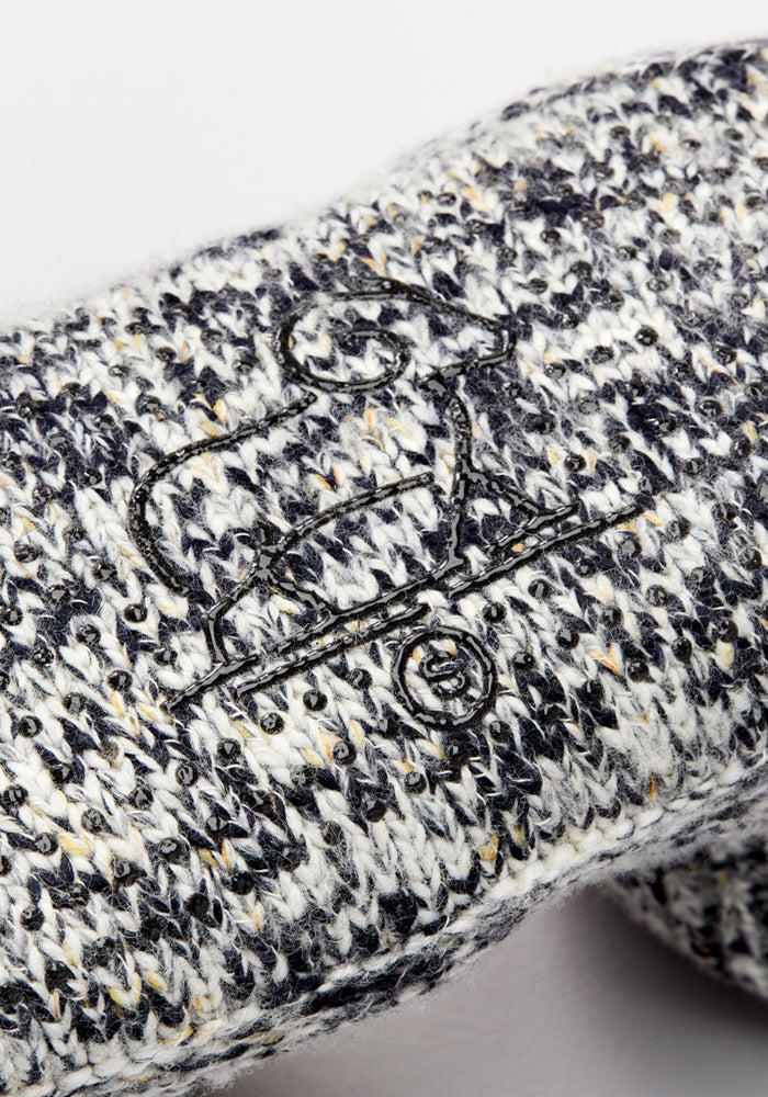 Close-up of a knitted gray and white fabric with a black embroidered dog on a skateboard, like the Woolx Men's Gripper Slipper Bootie in Speckled Stone, featuring cozy Merino wool and bottom grippers.