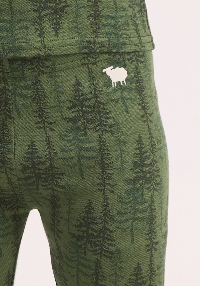 Close-up of Woolx Kids Explorer Base Layer Bottoms - Forest Friends, showing green fabric with a pine tree pattern and white sheep logo near the pocket—perfect cozy merino wool baselayer pants for kids.