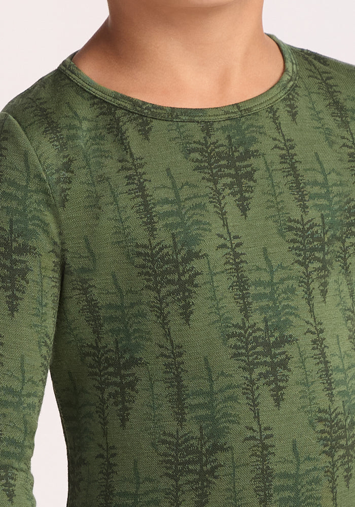 A close-up of a child wearing the Woolx Kids Explorer Base Layer Top - Forest Friends, featuring a dark green fern leaf pattern. Only the lower face, neck, shoulder, and upper chest are visible.