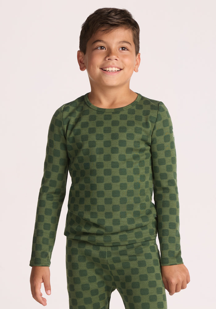 A smiling young boy stands against a plain light background, wearing the Woolx Kids Explorer Base Layer Top - Frog Hop, a green Merino wool long-sleeve that's breathable and perfect as a kids' wool thermal top. 