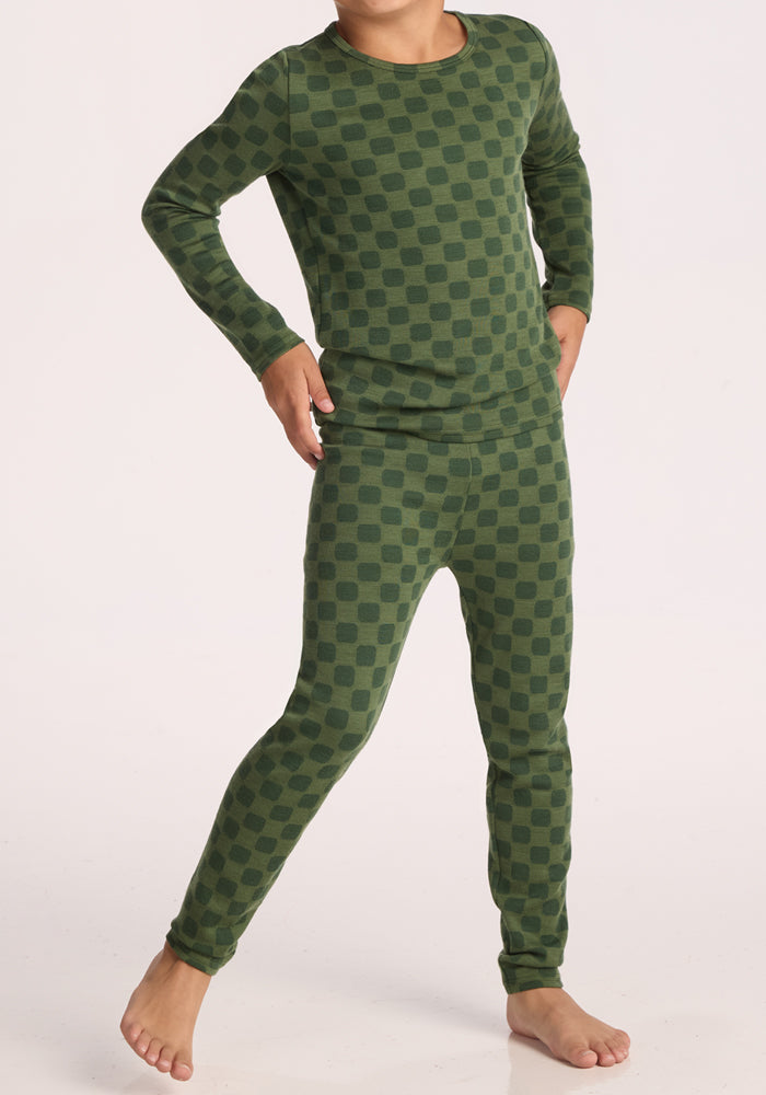 A child stands confidently in Woolx Kids Explorer Base Layer Bottoms - Frog Hop—ideal comfort for bedtime or layering over merino wool on chilly nights.