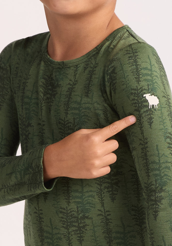 A child wears the Woolx Kids Explorer Base Layer Top - Forest Friends, featuring a green fern pattern and a white moose logo on the shoulder. Made from moisture-wicking Australian Merino wool, it offers all-day comfort. Only the upper body and arm are visible.