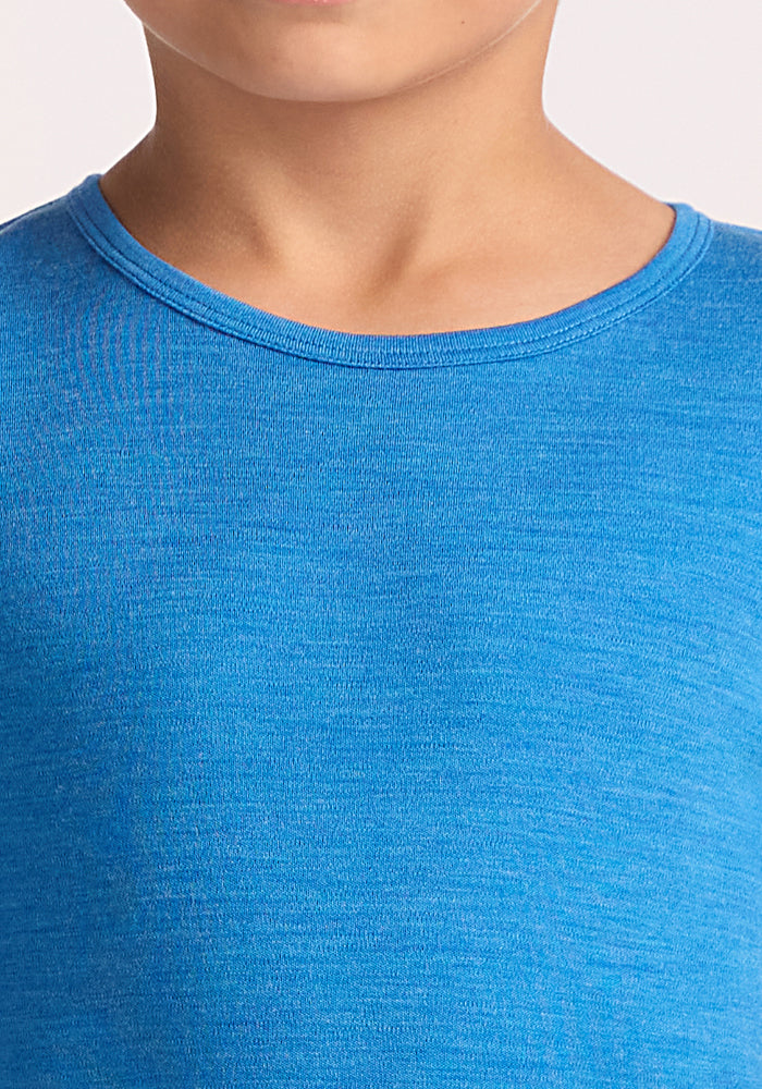 Close-up of a child wearing the Woolx Kids Explorer Base Layer Top in Blue Razz. The image highlights the crew neck and upper chest, with part of the lower face visible. Background is plain and light-colored.
