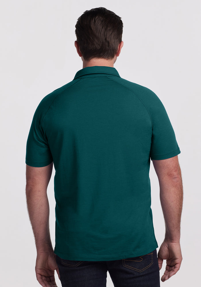 A man, seen from behind, wears the Woolx Summit Polo in Riverbank Green and dark jeans against a plain light background.