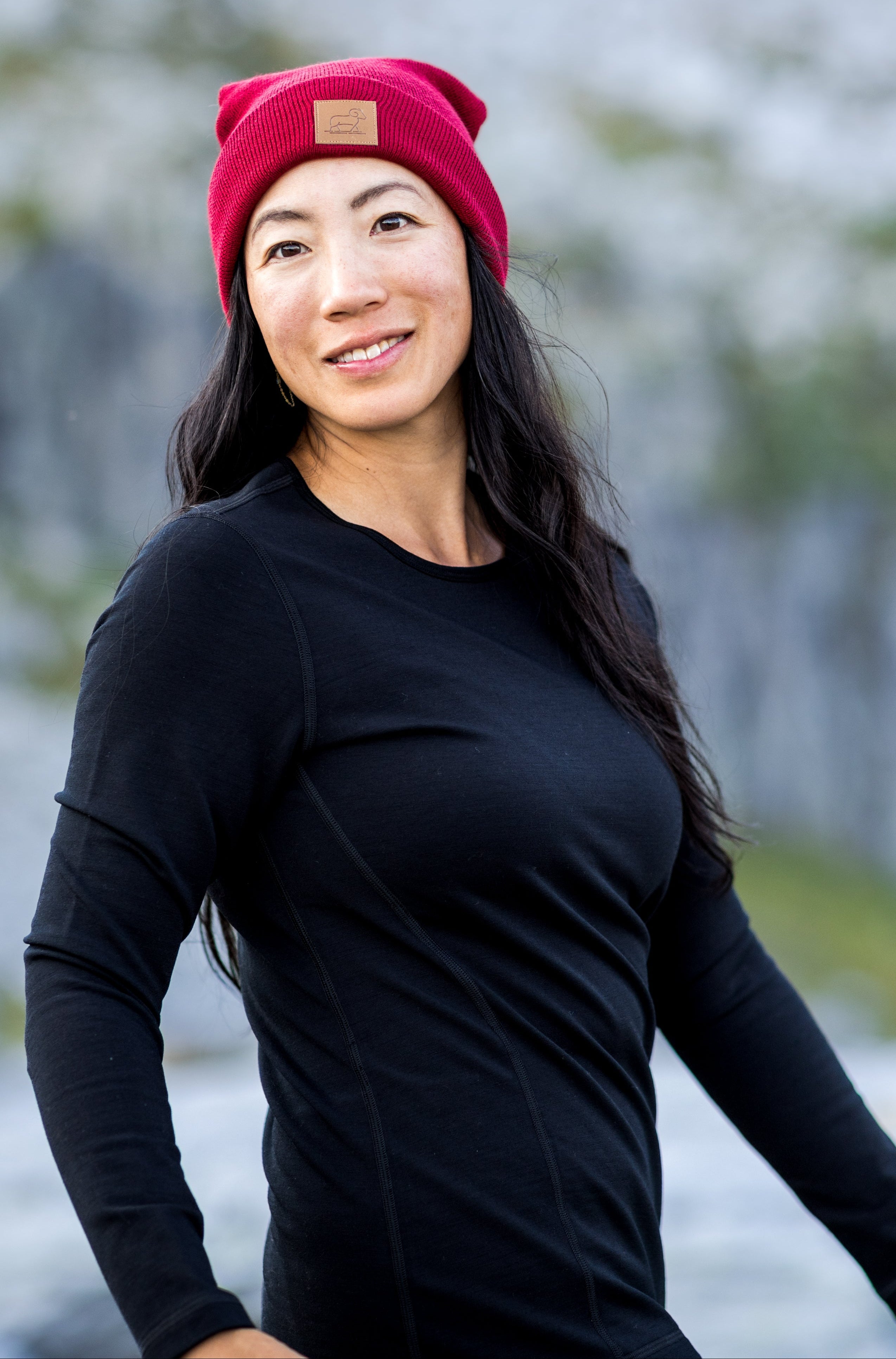Woman wearing a black long-sleeve shirt and red beanie standing in a natural setting with blurred background