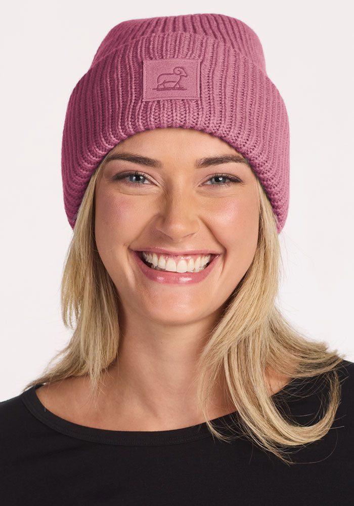 Smiling woman in Woolx Ria Chunky Beanie - Toasted Rose and black top, posed against a white background.