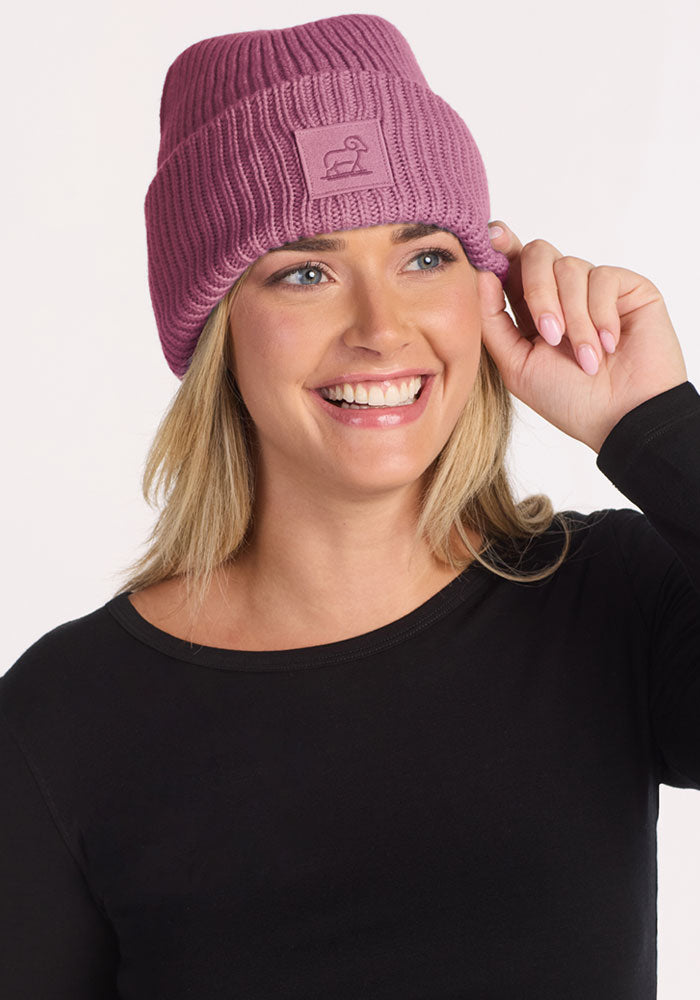 Smiling woman in the Woolx Ria Chunky Beanie in Toasted Rose, touching the brim of her cozy winter hat.