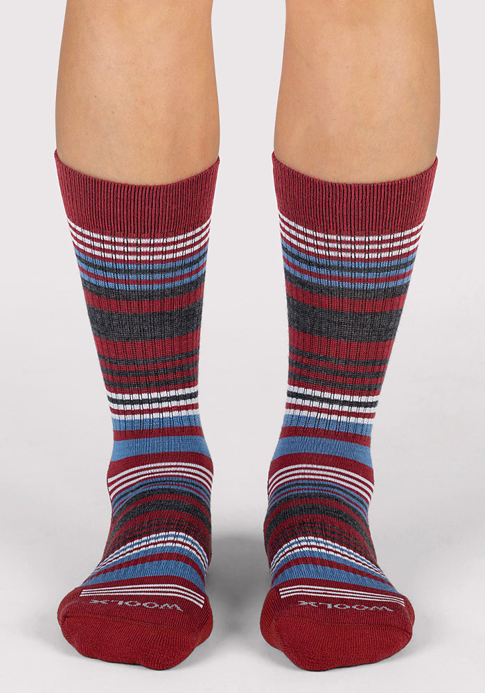 A pair of feet wearing Woolx Womens Everyday Crew Socks - Rhubarb Stripe, featuring red, blue, gray, black, and white ribbed stripes. These moisture-wicking crew socks offer a comfortable mid-calf fit against a plain light background.