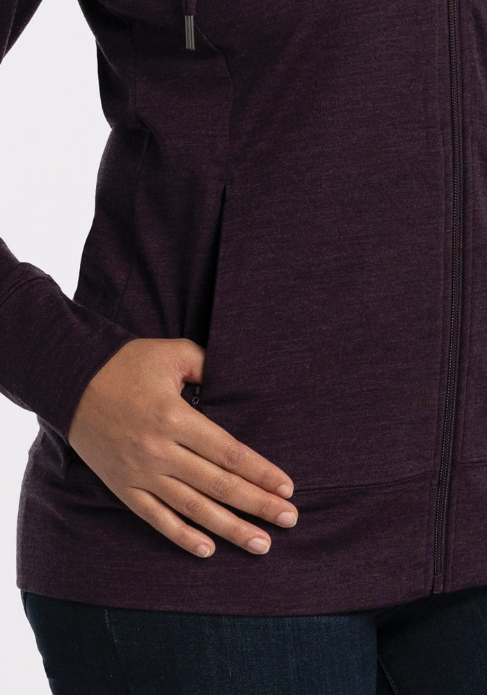 A person wears the Woolx Ryann Hoodie in Deep Plum, casually resting a hand in its pocket. This travel-ready, lightweight hoodie is styled with dark blue jeans against a plain white background.