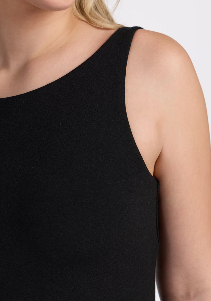 A close-up shows someone wearing the Woolx Adrienne Active Dress - Black, highlighting the sleeveless design and upper body details against a plain light background, with the face partially out of frame.
