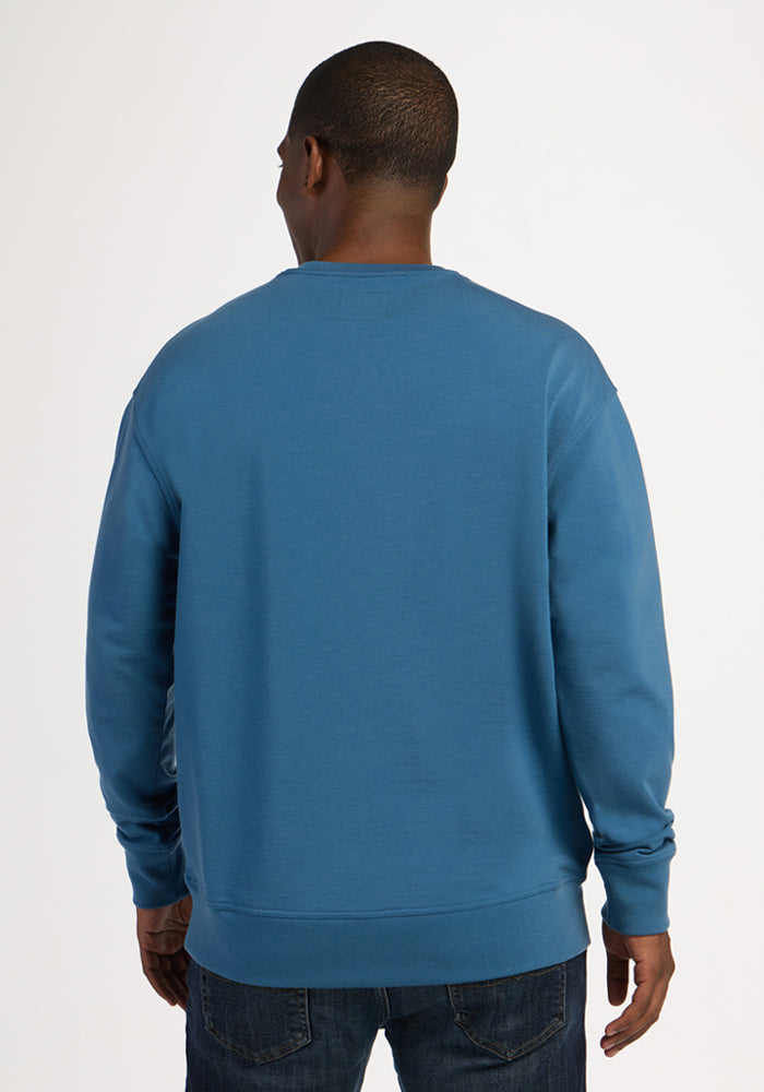 A person seen from behind wearing a Blue Ashes Miles Crewneck and dark jeans.