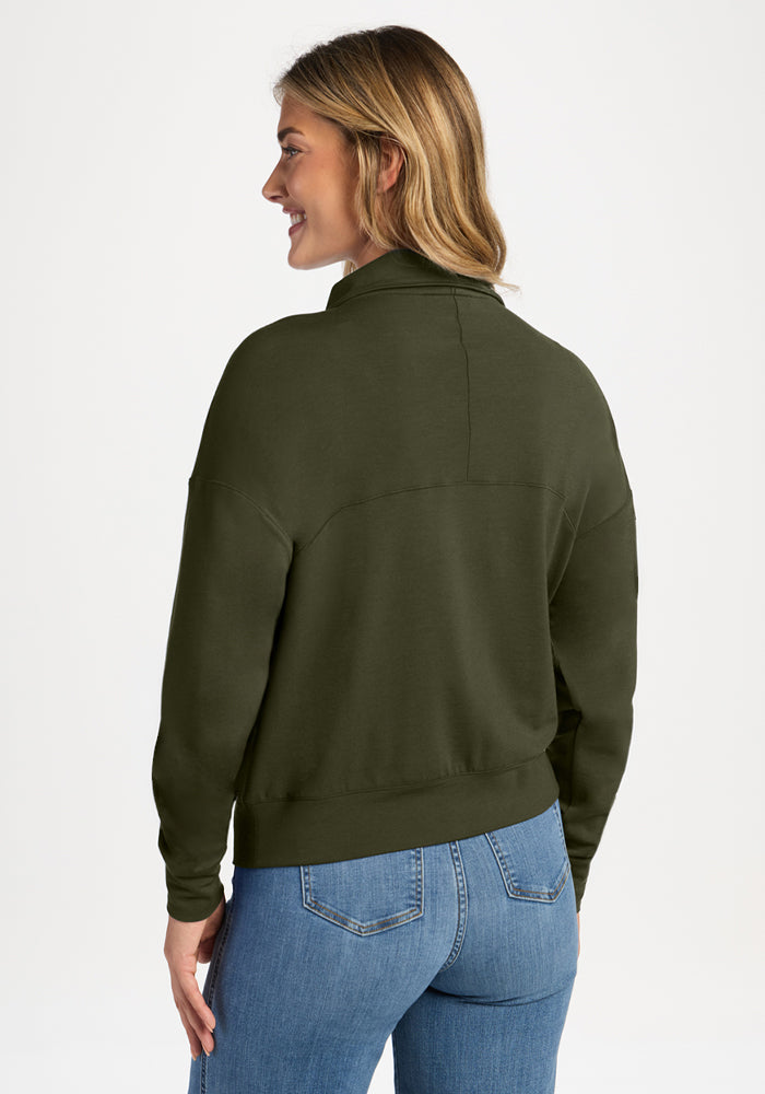 A woman seen from the back wearing an olive green Woolx Tori 1/4 Zip - Everleaf and jeans.