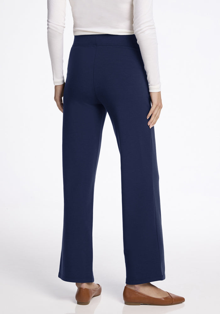 Woman stands, back view, in Woolx Ellie Wide Leg Pants - Ocean Cavern, white long sleeve, and brown flats on white.