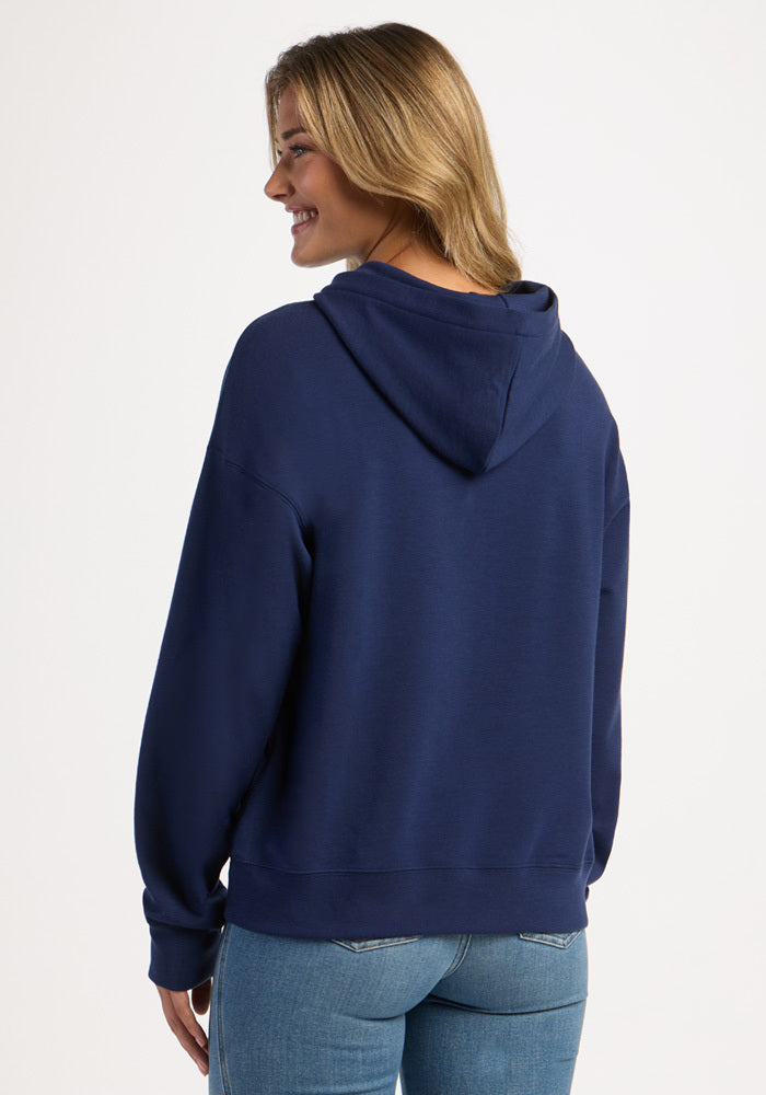 A woman seen from behind wearing a dark blue Woolx Genevieve Hoodie - Ocean Cavern and jeans.