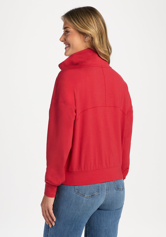 A woman seen from the back wearing a red Tori 1/4 Zip - Maraschino Cherry merino wool quarter-zip and blue jeans.