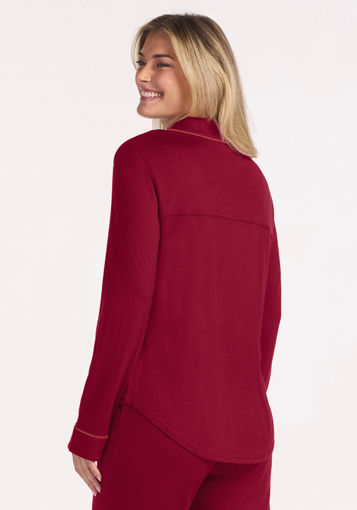 A smiling woman wears deep red, temperature-regulating Harper FeatherTouch® Pajama Set Merino wool pajamas with piping.