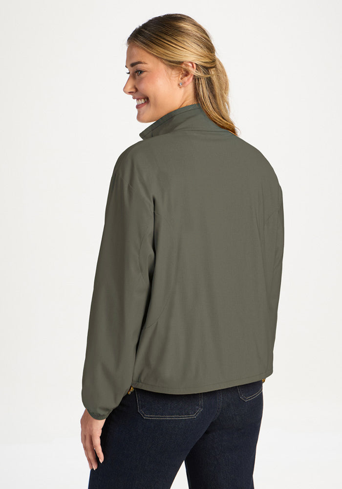 A woman seen from behind wearing a sage olive Cooper Windbreaker, a sage green throw-on with a customizable fit.